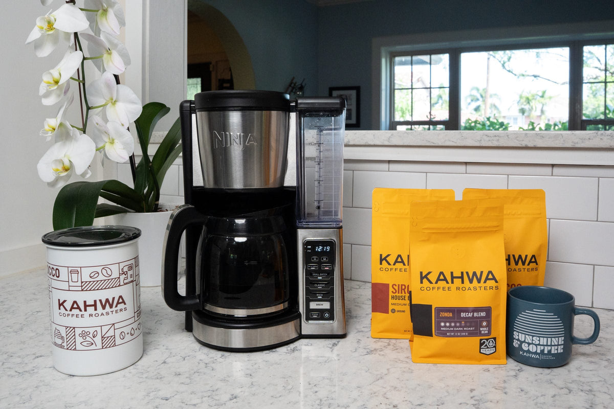 Kahwa coffee bags beside a drip coffee maker in a home kitchen