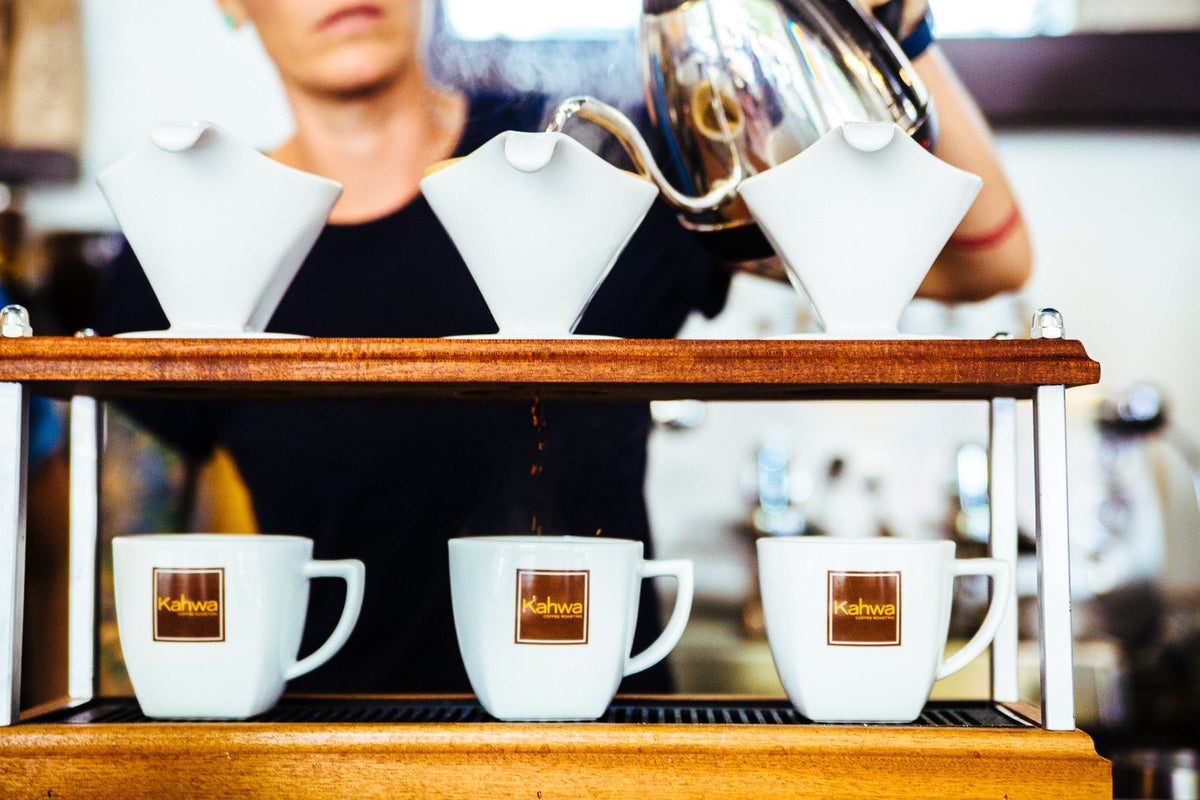 Barista pouring water over three pour over drippers into Kahwa mugs