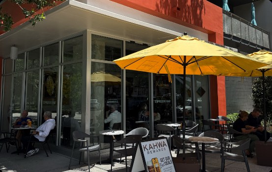 Guests seated under yellow umbrellas on a Kahwa Coffee cafe patio