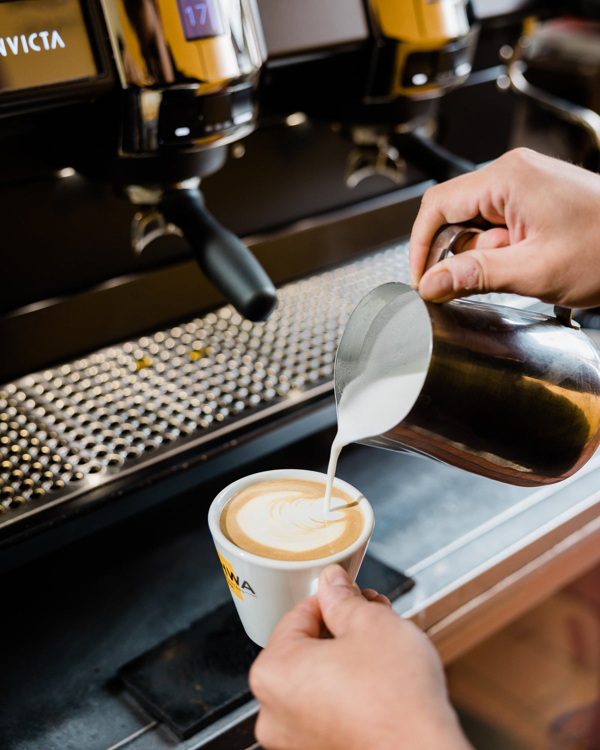 Kahwa barista pouring latte art into a Kahwa cup at the espresso machine